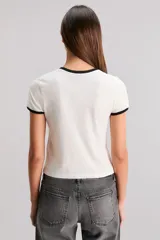 Remera blanca de calce slim, escote redondo y manga corta, con ribete negro en cuello y mangas. Estampa frontal de una frutilla roja con la frase "Bite Me".