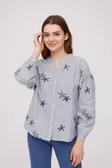 Camisa a rayas verticales blancas y celestes con bordado de estrellas de mar azules, de corte holgado, cuello en V y mangas largas abullonadas.