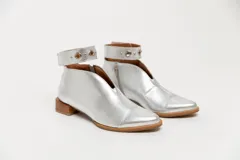 Botín plateado de cuero con taco bajo de madera, corte en V en el empeine, pulsera con detalles metálicos y cierre lateral.