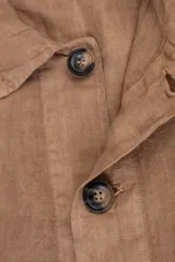 Campera color marrón claro estilo sobrecamisa confeccionada en lino premium. Cuenta con cuello clásico, cierre frontal con botones, un bolsillo de parche en el pecho y dos bolsillos de parche en la parte inferior.