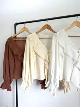 Blusa color blanco confeccionada en bambula liviana, con textura suave y caída fluida, escote en V con volados y mangas largas con puños elásticos.