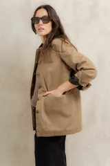 Campera color beige con cuello de corderito negro, cierre con botones, bolsillos laterales y puños con detalle de cuero sintético negro.