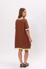 Vestido corto marrón de tejido de punto con cuello redondo y mangas cortas. Presenta ribetes en color celeste en el cuello, rosa en las mangas y amarillo en el ruedo.