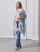Kimono tejido con estampado floral multicolor, terminación de ruedo con borlas y mangas cortas con borde celeste.
