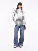 Polera blanca con rayas horizontales negras, cuello alto y mangas largas.