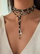 Collar doble con tiras de gamuza y pelotitas metálicas, ajustable y versátil para diversas formas de uso.