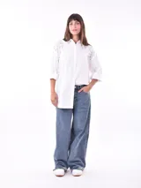 Camisa blanca de corte oversize con cuello clásico, cierre frontal con botones y mangas largas con puños abotonados. Presenta detalle de encaje en los hombros.