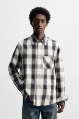 Camisa de hombre regular fit confeccionada en tejido de algodón a cuadros en tonos azul oscuro y verde oliva. Tiene cuello solapa, manga larga con puños abotonados, bolsillo de plastrón en el pecho y cierre frontal con botones.
