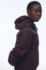 Campera con capucha color borgoña, con cierre frontal y bolsillos tipo canguro. Confeccionada en felpa con interior cepillado suave, hombros caídos, capucha forrada con cordón para ajustar y puños y bajo en punto acanalado.