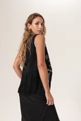 Chaleco negro de gamuza con flecos y bordados blancos en la parte frontal.