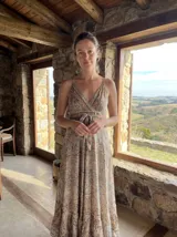 Vestido largo estampado con tirantes finos y escote en V cruzado. Presenta un patrón paisley en tonos tierra, beige y azul, con un lazo ajustable en la cintura y un ruedo con volado.