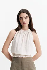 Blusa color crudo sin mangas, con cuello halter y elástico en el cuello y la cintura.