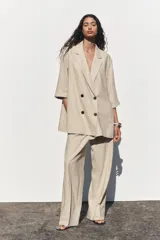 Pantalón color beige de lino, de tiro alto con cintura elástica, bolsillos laterales ocultos en costura y pernera ancha.