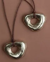 Collar con dije dorado irregular con agujero central, colgando de cordón negro ajustable.