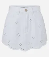 Short pollera corto de jeans blanco con bordados calados (cutout) y bajo festoneado. Presenta trabillas en la cintura y cierre tradicional.