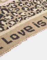 Bufanda tejida de forma triangular, con estampado de corazones en la parte superior, animal print en el centro y la frase "Love is Love" en los bordes.