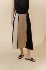 Falda midi de lino y algodón con paneles verticales en color beige, negro y tostado. Diseño portafolio con cruce, abrochada con botones y broches de presión regulables. Detalles desflecados en los cortes verticales y bolsillo escondido en el lateral derecho.