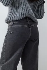 Jean wide leg de denim gris oscuro, con tiro medio, cierre de botón y cremallera. Presenta un diseño de pierna ancha con costuras decorativas en la parte delantera y ruedo deshilachado.