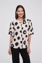 Blusa de manga corta con estampado de manchas negras y azules sobre fondo crema, cuello mao y cierre frontal con botones.
