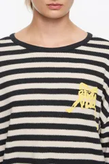 Camiseta de tejido de punto de manga larga, con patrón de rayas horizontales anchas en blanco crudo y negro. Presenta cuello redondo con ribete negro y un pequeño bordado amarillo en el pecho.