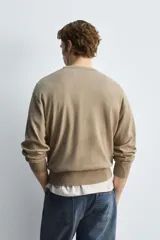 Jersey de hombre color beige, de corte relaxed fit, tejido en hilatura con algodón y ramio. Tiene cuello pico, manga larga y acabados en rib.