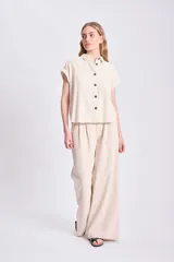 Camisa color crudo de lino, con cuello clásico, manga corta con dobladillo y cierre frontal con botones negros.