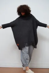 Poncho tejido de lana color gris oscuro, con cuello alto y flecos en el ruedo.