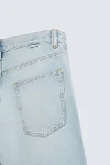 Bermuda de denim de algodón, color gris claro lavado, de corte ancho (baggy fit) y largo hasta la rodilla. Presenta cinco bolsillos y cierre frontal con cremallera y botón.