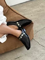 Sueco de cuero negro con detalle de apliques metálicos triangulares plateados.