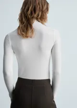 Camiseta blanca de cuello alto y manga larga, corte ajustado.