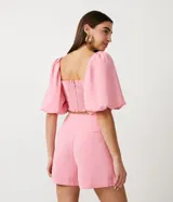 Blusa cropped color rosa con escote cuadrado y mangas cortas abullonadas.