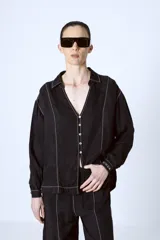 Blusa negra con botones, cuello camisero y mangas largas con puños. Presenta pespuntes blancos en contraste.
