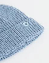 Gorro de lana tejido color rosa viejo, con pompón en la parte superior y etiqueta metálica con logo en el borde.