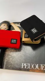 Billetera corta con cierre alrededor y tapa, confeccionada en tela capitoneada. Incluye varias reparticiones con tarjeteros y bolsillos internos, y una correa de mano desmontable. Disponible en negro, rojo y dorado.