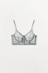 Bralette con aros de escote corazón y tirantes finos ajustables. Detalle de aplicación de tejido combinado en guipur. Varillas interiores que realzan y estilizan la figura. Cierre en espalda con ganchos metálicos.
