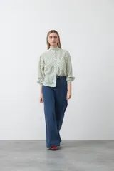 Camisa de viscosa blanca con estampa de lunares negros. Presenta cuello alto con volado y botonadura frontal, mangas largas con puños abullonados y frunces bajo el busto.