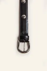 Cinturón de cuero negro con tachas metálicas circulares y hebilla plateada.