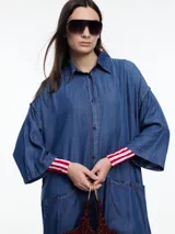 Vestido camisero largo de denim liviano de lyocell azul, de silueta relajada, mangas 3/4 amplias y hombro caído. Cuenta con bolsillos grandes aplicados en el frente, tajos laterales y botones a contratono.
