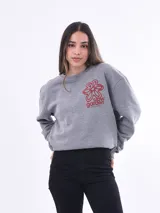 Buzo de tejido de punto color gris melange, con cuello redondo y manga larga. Presenta un estampado frontal en rojo que incluye una flor estilizada y el texto "slow garden there's no hurry".