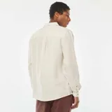 Camisa de lino color beige claro, de corte regular, con cuello clásico y mangas largas con puños abotonados.