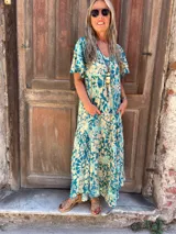 Vestido largo de seda, fluido y amplio, con mangas cortas y bolsillos laterales. Presenta un estampado en tonos turquesa y beige/crema.