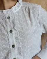 Camisa a rayas verticales color beige y blanco, de corte holgado, con cuello con volados, cierre parcial con botones y mangas largas con puños abotonados.