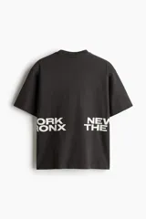 Remera negra de corte holgado con cuello redondo y mangas cortas. Estampado frontal con la inscripción "ORK XON NEW THE".