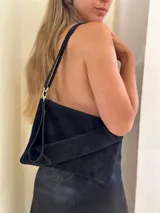 Sobre/cartera de gamuza color marrón oscuro, con diseño de solapa diagonal. Incluye una correa larga para usar al hombro o como bandolera, y una correa corta para la muñeca, ambas desmontables.