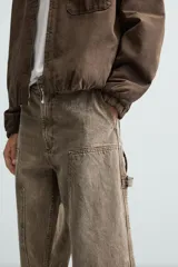 Pantalón gris de corte relaxed fit, con cinco bolsillos, efecto lavado, aplicación de tira y bolsillo multifunción en perneras. Cierre frontal con cremallera y botón.