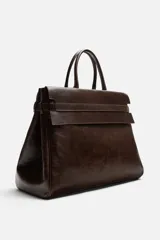 Bolso de mano extragrande color marrón oscuro, fabricado en piel de alta calidad. Tiene un compartimento principal con cierre magnético, un bolsillo interior con cremallera y un bolsillo secundario con solapa y cinta. Las asas son de piel.