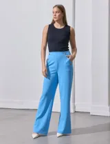 Pantalón largo de crepe elastizado color verde, de corte recto, con bolsillos delanteros y apliques de botones metálicos.