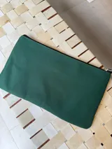 Sobre tipo cartuchera color borgoña, de lona con terminaciones en cuero marrón. Tiene cierre superior y aplique de cuero con el logo de la marca.