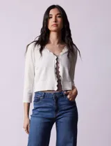 Cardigan tejido en hilado fino color blanco, marca Cable & Gauge. Abertura central con broche interno y terminación ondulada.