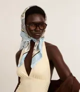 Pañuelo rectangular de satén con estampado paisley en tonos blanco, azul claro y beige. El pañuelo se anuda bajo la barbilla, cubriendo la cabeza.